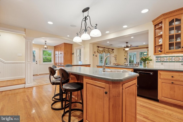 kitchen featuring black dishwasher, light wood-type flooring, a kitchen island with sink, brown cabinetry, and a sink