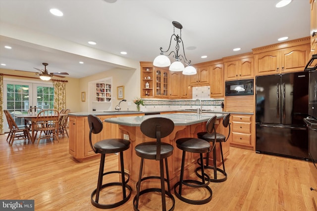kitchen featuring black appliances, a sink, a center island, light wood-style floors, and a kitchen bar