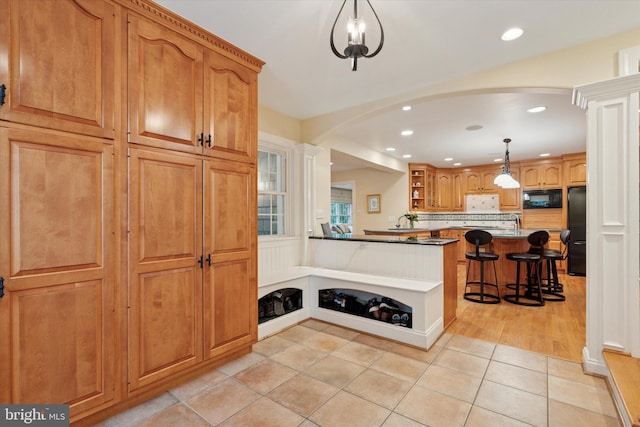 kitchen with black appliances, a kitchen breakfast bar, open shelves, arched walkways, and light tile patterned flooring