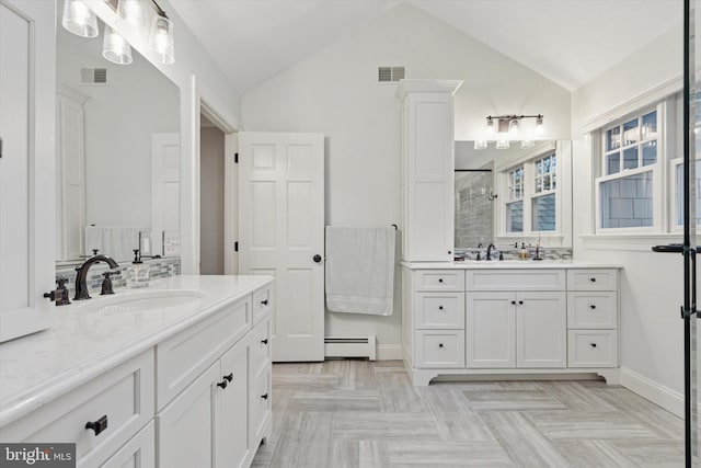 bathroom with a shower stall, lofted ceiling, a baseboard heating unit, two vanities, and baseboards