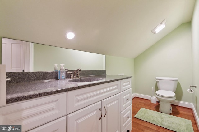 bathroom with vaulted ceiling, toilet, wood finished floors, vanity, and baseboards