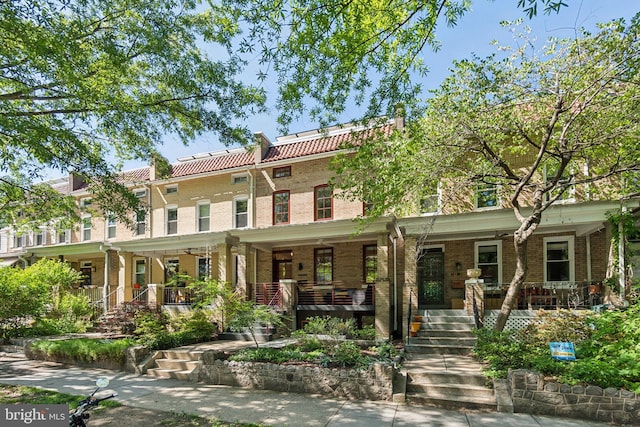 townhome / multi-family property featuring covered porch, a tile roof, brick siding, and stairs