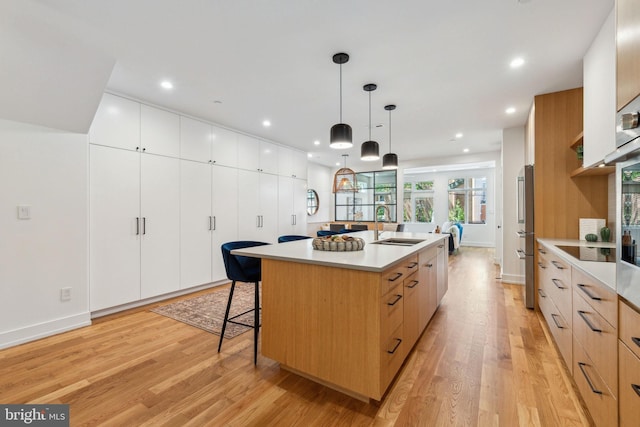 kitchen featuring modern cabinets, a sink, a spacious island, light wood finished floors, and recessed lighting