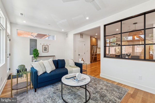 living room with wood finished floors, electric panel, ceiling fan, baseboards, and recessed lighting