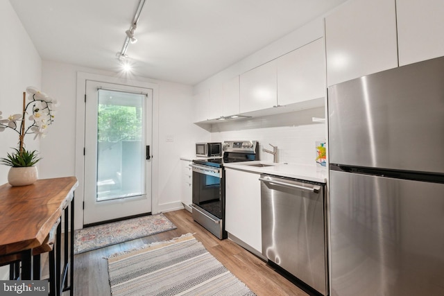 kitchen with stainless steel appliances, light wood-style floors, white cabinets, track lighting, and a sink