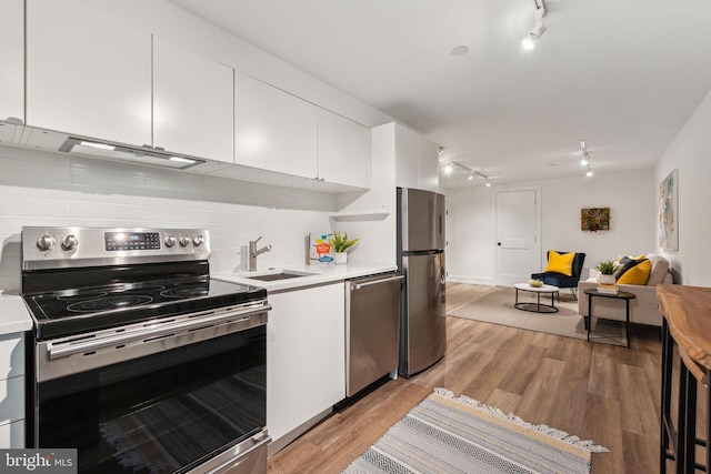 kitchen with appliances with stainless steel finishes, a sink, track lighting, and light countertops