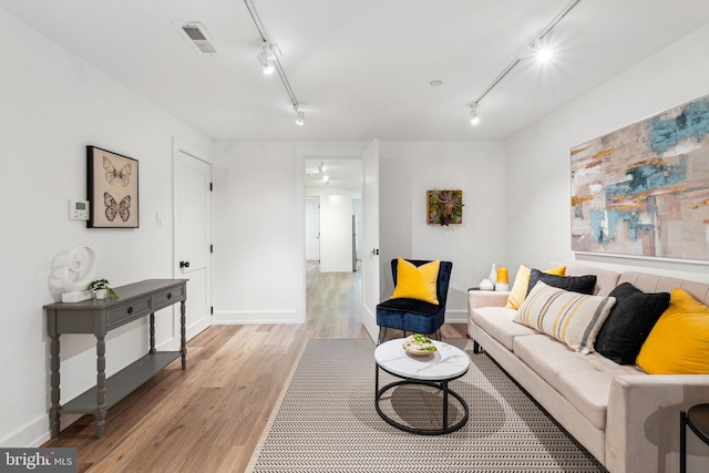 living area featuring rail lighting, attic access, light wood-style floors, and baseboards