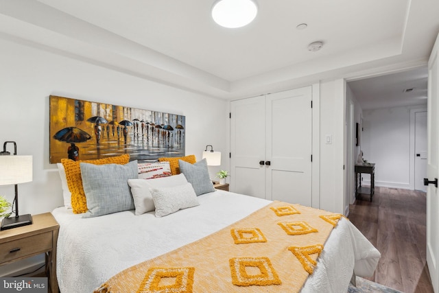bedroom with wood finished floors, a closet, and a tray ceiling
