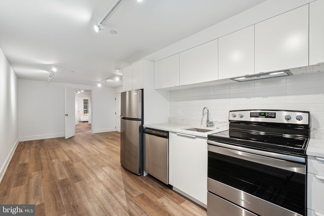 kitchen featuring appliances with stainless steel finishes, a sink, decorative backsplash, light wood-style flooring, and white cabinets