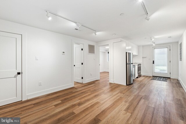 unfurnished living room with rail lighting, light wood-style floors, and baseboards