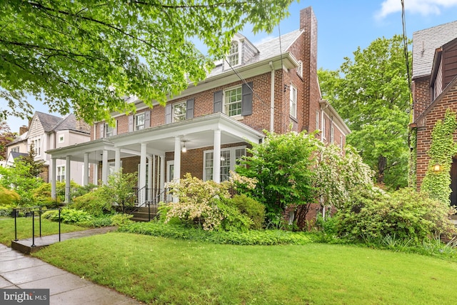 view of front of home featuring brick siding, a chimney, a front lawn, and covered porch