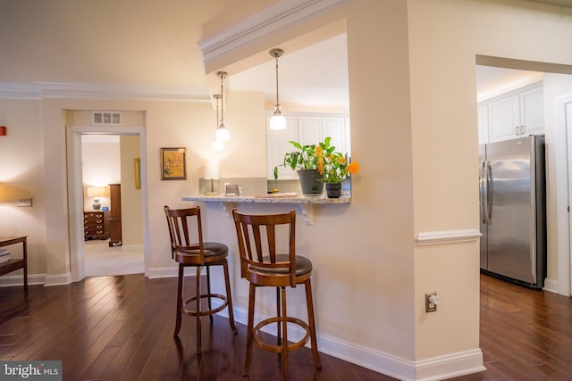 kitchen with freestanding refrigerator, a kitchen bar, dark wood-style floors, white cabinets, and crown molding