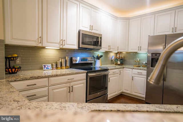 kitchen featuring stainless steel appliances, backsplash, white cabinets, and light stone counters