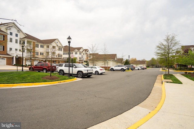 view of asphalt street with a residential view, street lights, curbs, and sidewalks