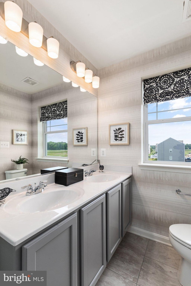 full bath featuring toilet, double vanity, tile patterned flooring, and wallpapered walls