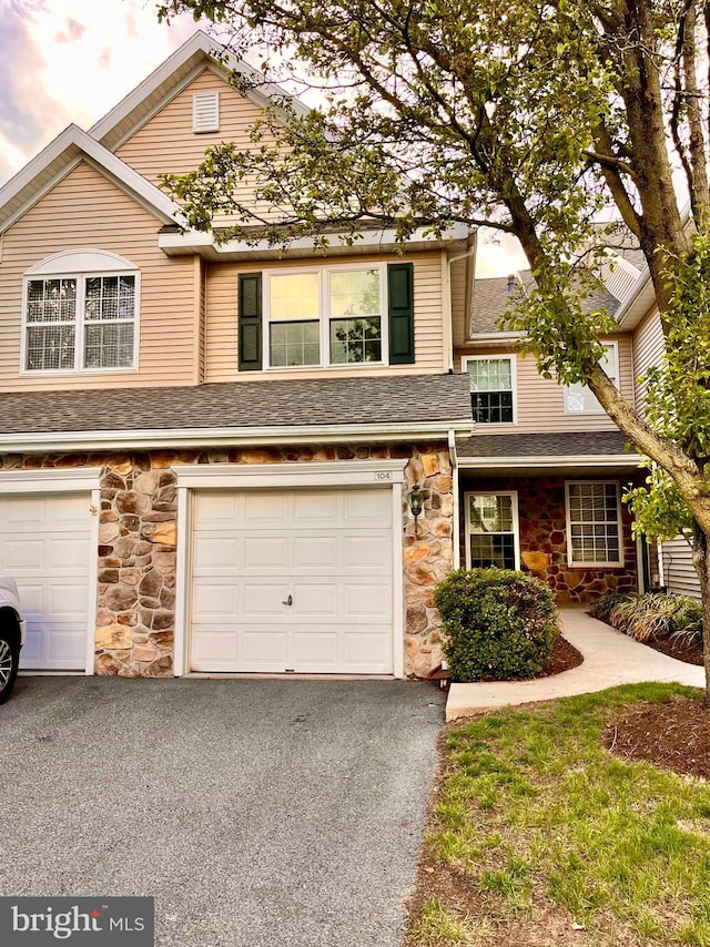 multi unit property with stone siding, driveway, a garage, and roof with shingles