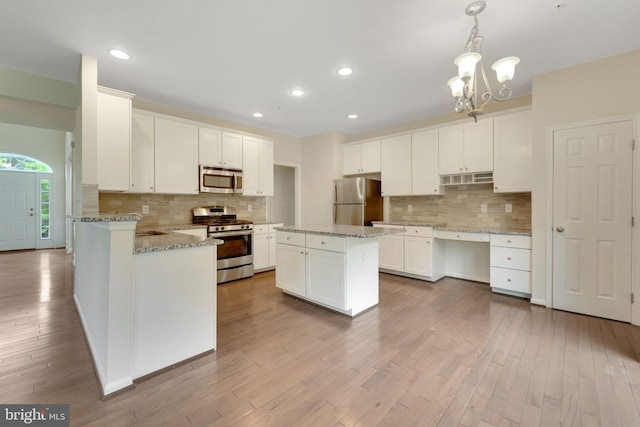 kitchen with stainless steel appliances, decorative backsplash, white cabinets, wood finished floors, and a chandelier