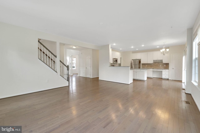unfurnished living room with a chandelier, plenty of natural light, dark wood finished floors, stairs, and recessed lighting