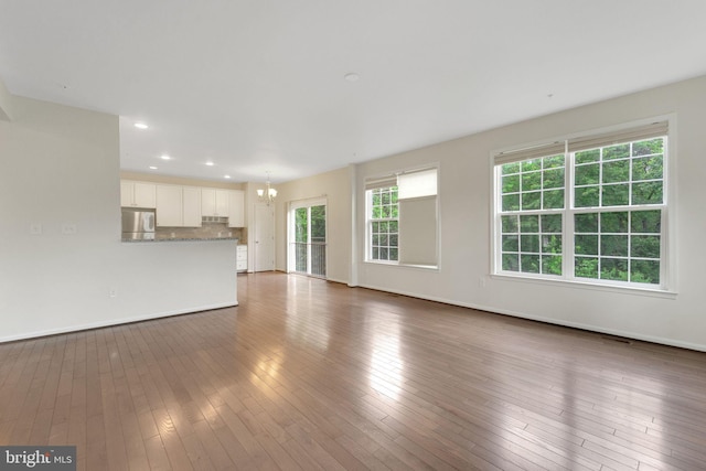 unfurnished living room with a chandelier, wood-type flooring, baseboards, and recessed lighting