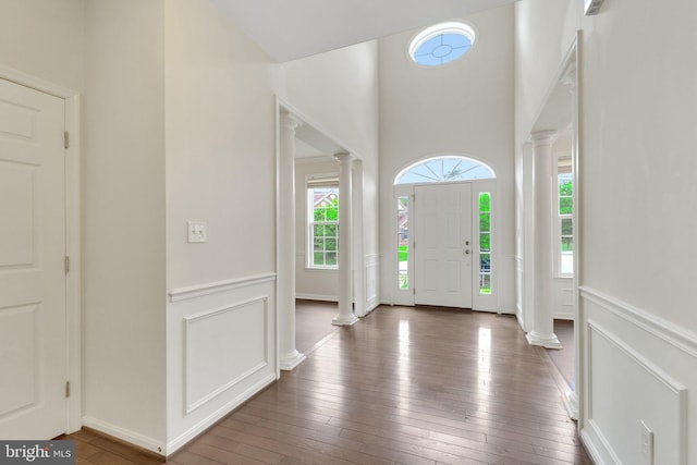 foyer featuring decorative columns, wood-type flooring, a wainscoted wall, and a high ceiling