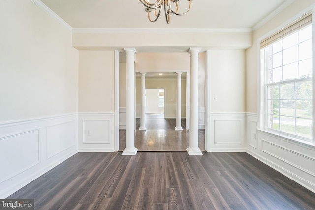 unfurnished dining area featuring plenty of natural light, ornate columns, dark wood-style floors, crown molding, and wainscoting