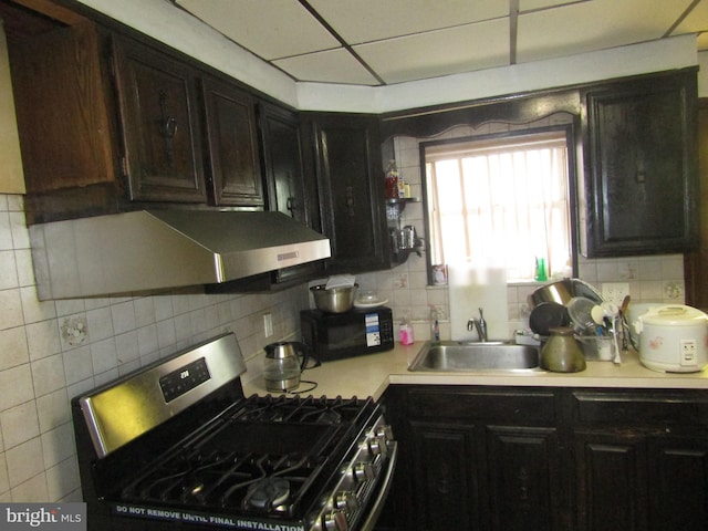 kitchen featuring stainless steel gas range oven, black microwave, decorative backsplash, a sink, and light countertops