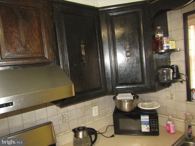 kitchen featuring black microwave, decorative backsplash, dark brown cabinets, and light countertops