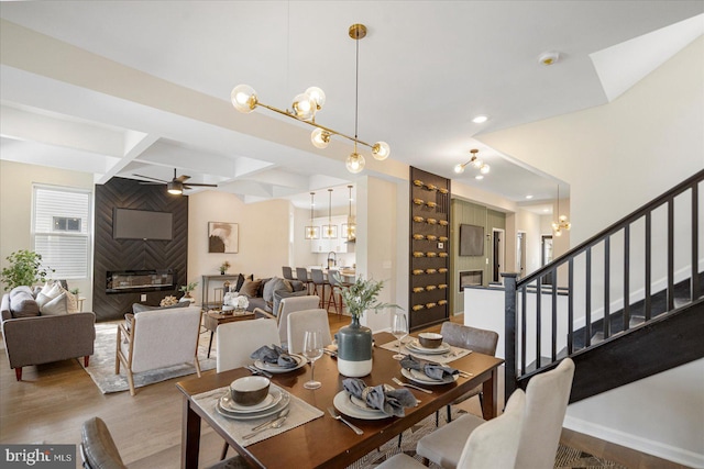 dining room with a ceiling fan, a chandelier, coffered ceiling, stairs, and wood finished floors