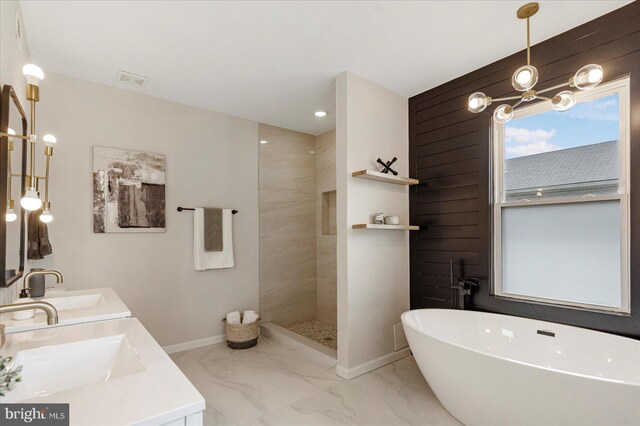 bathroom featuring marble finish flooring, a freestanding bath, a walk in shower, double vanity, and baseboards