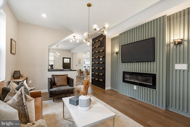 living area featuring wood finished floors, a chandelier, baseboards, and a glass covered fireplace