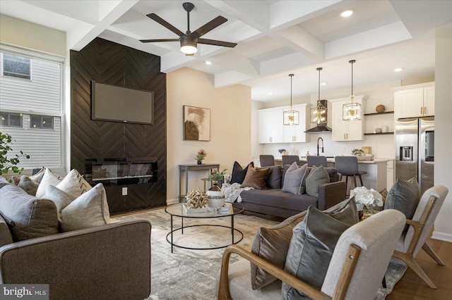 living area featuring coffered ceiling, a ceiling fan, beamed ceiling, recessed lighting, and a large fireplace