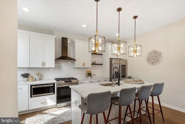 kitchen featuring wall chimney range hood, appliances with stainless steel finishes, decorative backsplash, a center island with sink, and a kitchen bar