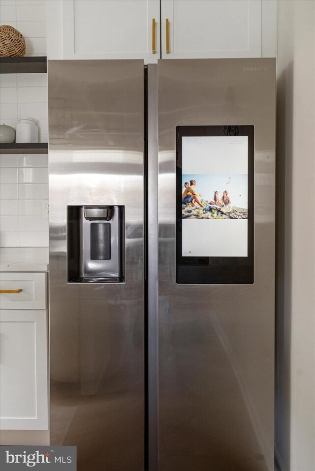 kitchen view of stainless steel fridge, open shelves, white cabinets, and light countertops