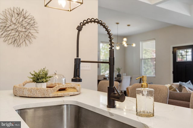 detailed view of a chandelier, light stone countertops, a sink, and pendant lighting