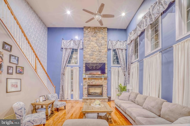 living area with wood finished floors, ceiling fan, a stone fireplace, a towering ceiling, and recessed lighting