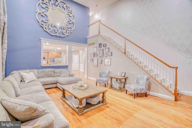 living room with wood finished floors, stairs, a towering ceiling, baseboards, and wallpapered walls
