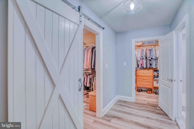 hall with a barn door, light wood-style floors, and baseboards