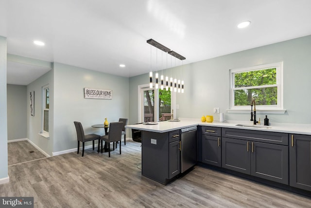 kitchen with a sink, dishwasher, a peninsula, light wood-style flooring, and light countertops