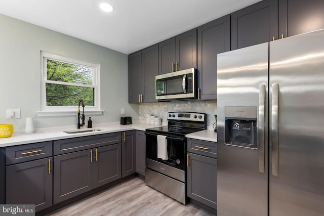 kitchen featuring appliances with stainless steel finishes, a sink, recessed lighting, light wood-type flooring, and light countertops