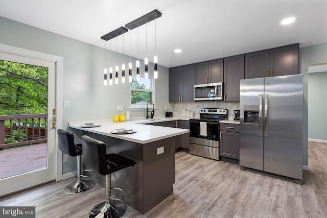 kitchen featuring stainless steel appliances, a peninsula, a sink, light countertops, and recessed lighting