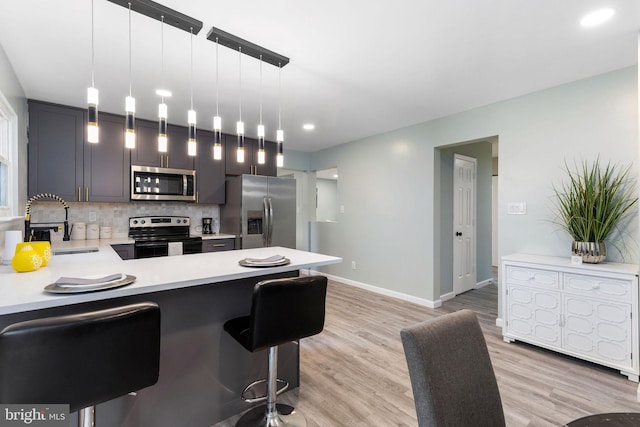 kitchen with stainless steel appliances, light countertops, a sink, light wood finished floors, and a kitchen bar