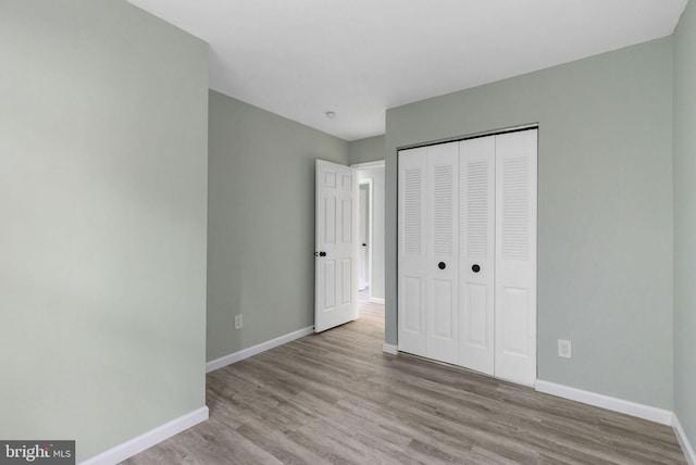 unfurnished bedroom featuring baseboards, wood finished floors, and a closet