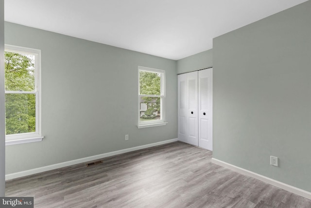 unfurnished bedroom with multiple windows, wood finished floors, baseboards, and a closet