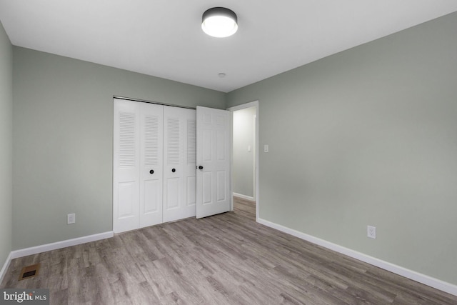 unfurnished bedroom with wood finished floors, baseboards, and a closet