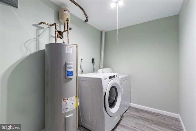laundry room featuring water heater, washing machine and clothes dryer, light wood-type flooring, baseboards, and attic access