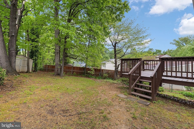 view of yard with fence, a deck, a storage unit, and an outbuilding