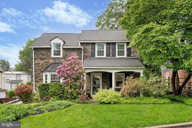 view of front of home with stone siding, a front yard, and roof with shingles