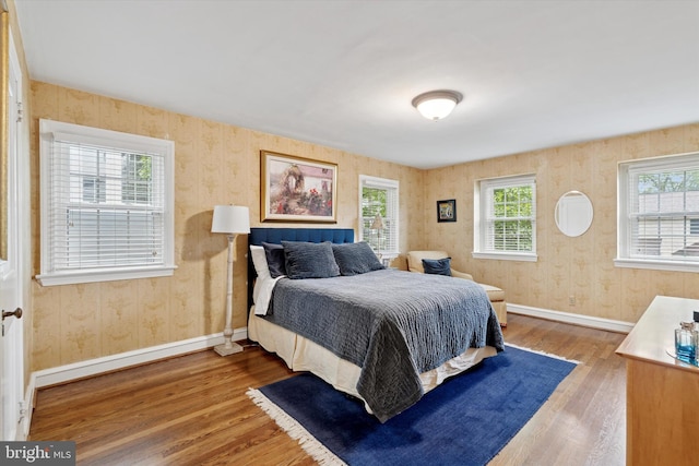 bedroom with wallpapered walls, wood finished floors, multiple windows, and baseboards