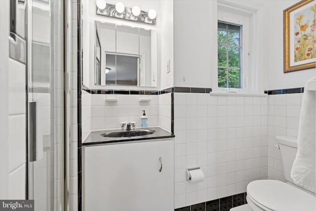 bathroom featuring tile walls, toilet, a shower with door, vanity, and a wainscoted wall