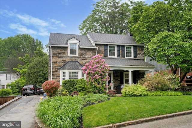 view of front of home with stone siding, a front yard, and a porch